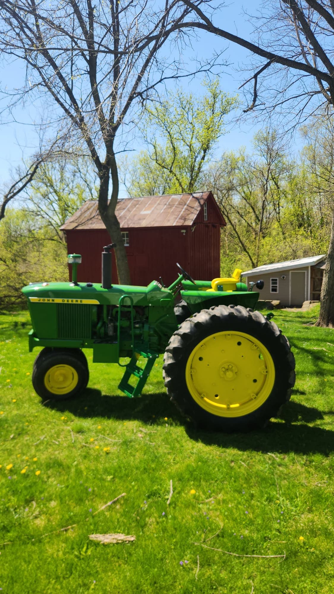 Restored John Deere 3010 parked in front of a red barn after paint and finish work